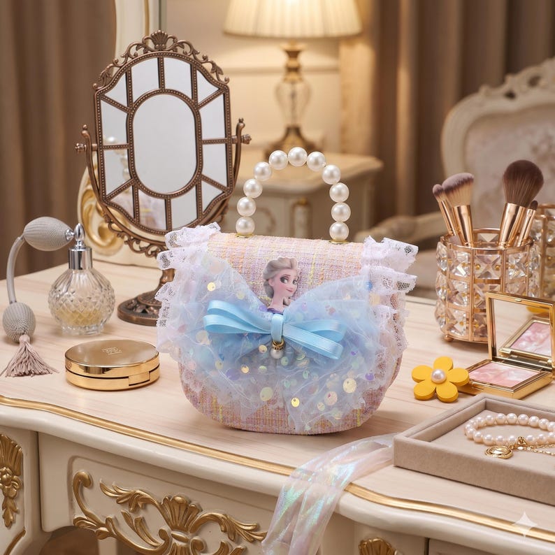 K&ouml;nnte beinhalten: Kleine, hellrosa Handtasche mit Perlenhenkel und blauer Schleife. Die Tasche zeigt ein Cartoon-Bild einer Prinzessin und ist mit Pailletten und Spitze verziert. Die Tasche steht auf einem Schminktisch.