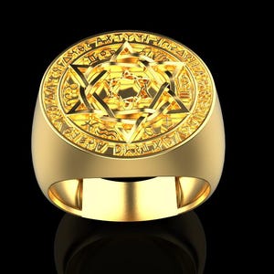May include: A gold ring with an elaborate design. The ring showcases a six-pointed star at its centre, enclosed by a circular frame with detailed patterns and symbols. The ring is set against a black backdrop.