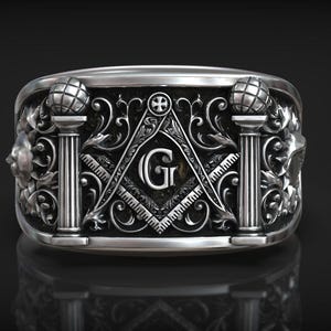 May include: Silver-toned ring featuring Masonic symbols. The ring has a detailed design with pillars, a compass, a square, and the letter "G". Decorative elements include floral patterns and globe-topped columns. The ring is displayed against a dark background.