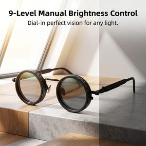 Op de afbeelding: Zwarte ronde bril met instelbare helderheidsregeling. De bril heeft een uniek ontwerp met een draaiknop om de helderheid aan te passen. De tekst "9-Level Manual Brightness Control" en "Dial-in perfect vision for any light" is zichtbaar.