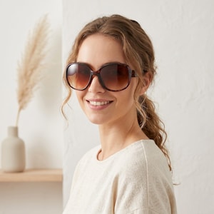 Puede incluir: Gafas de sol de gran tamaño con montura carey y lentes degradadas marrones. La persona lleva una camiseta de color claro. La imagen está tomada en interiores con un fondo neutro.