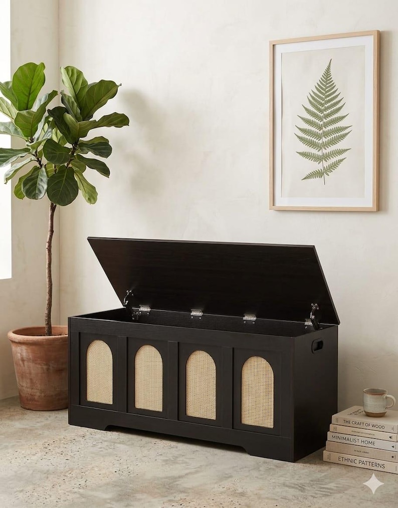 May include: A black wooden storage chest with a hinged lid, featuring four arched panels with woven cane inserts. A potted plant and a framed fern print are visible. The chest is approximately 122 cm wide.