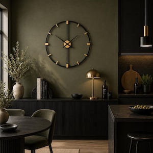 May include: A large circular wall clock featuring a black metal frame with gold-toned accents at each hour marker. The clock has thin black hands and a central gold-toned circular hub, mounted on a dark olive green wall above a black sideboard.