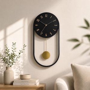 May include: A wall clock featuring a circular black face with gold-coloured numerals and thin black hands. The clock is encased in a black oval frame with a gold-coloured pendulum suspended from the centre, creating a vertical, elongated design.