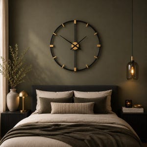 May include: A large circular wall clock featuring a thin black metal frame with gold-toned accents at the hour markers and center. The clock has two slender black hands and a vertical bar design that extends from the center to the top and bottom.