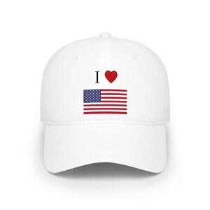 Könnte beinhalten: Weiße Baseballkappe mit dem Text "I ♥" über einer Grafik der amerikanischen Flagge. Das Design der Flagge umfasst rote und weiße Streifen und ein blaues Quadrat mit weißen Sternen. Ein lässiges Accessoire.