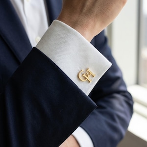 Peut inclure: Boutons de manchette dorés avec les initiales "GF" sur une manchette de chemise blanche, assortis à un costume bleu marine. Ces boutons de manchette présentent un design classique et élégant, idéal pour les tenues formelles.