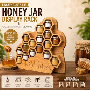Puede incluir: Un expositor de madera con forma de panal y el texto Wild Hives grabado en la parte frontal. El soporte cuenta con múltiples compartimentos hexagonales que contienen pequeños tarros de cristal llenos de miel. Diseño para corte láser.