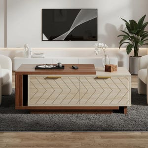 May include: A modern coffee table with a two-tone design. The top is a dark wood, and the lower section features a light wood with a chevron pattern. It has gold-colored handles and sits on a dark wood base. A TV is mounted on the wall in the background.