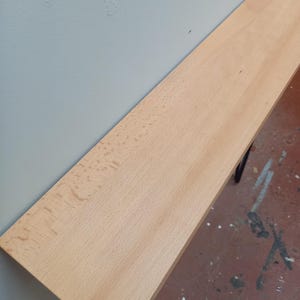 Peut inclure: Une &eacute;tag&egrave;re en bois de couleur claire, d'environ 122 cm de long, est fix&eacute;e au mur. L'&eacute;tag&egrave;re a une surface lisse et est soutenue par des supports en m&eacute;tal fonc&eacute;. Le mur est peint en gris clair et le sol est rouge mouchet&eacute;.