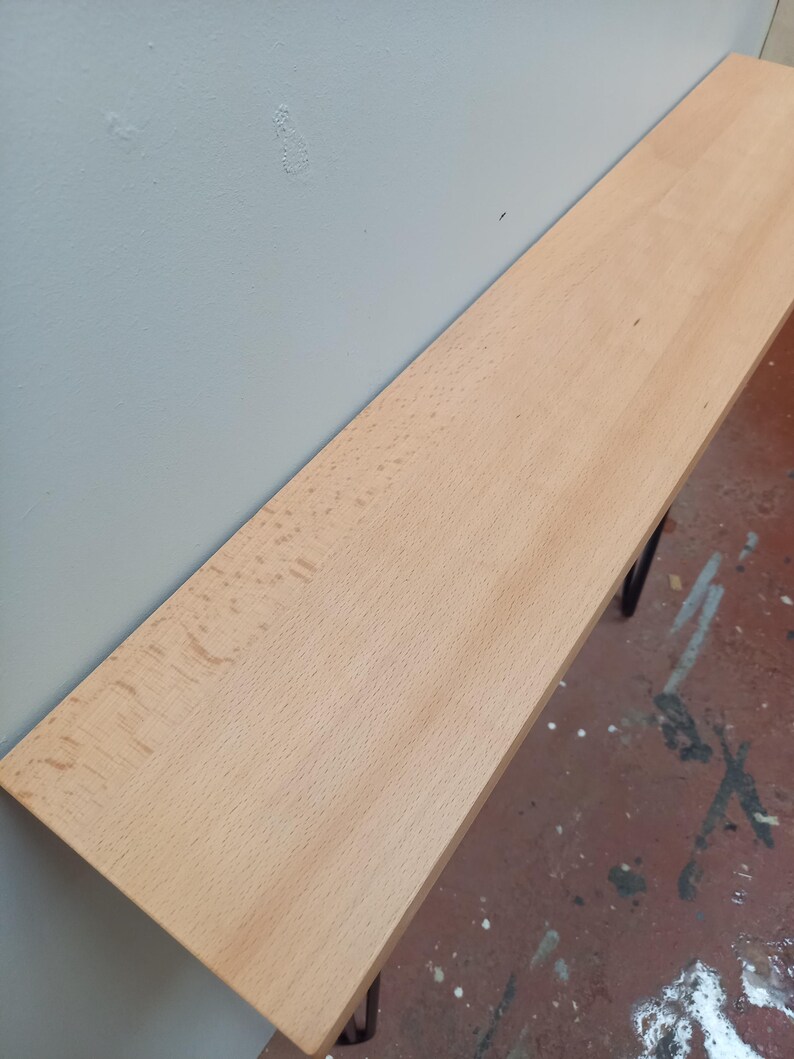 Peut inclure: Une &eacute;tag&egrave;re en bois de couleur claire, d'environ 122 cm de long, est fix&eacute;e au mur. L'&eacute;tag&egrave;re a une surface lisse et est soutenue par des supports en m&eacute;tal fonc&eacute;. Le mur est peint en gris clair et le sol est rouge mouchet&eacute;.