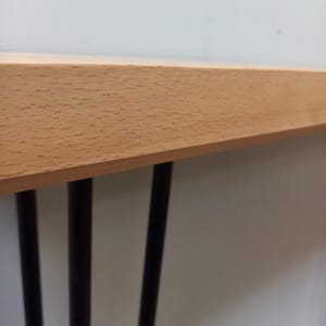 Peut inclure: Une table en bois clair avec trois pieds en m&eacute;tal noir. Le plateau a une finition en grain de bois naturel. Les pieds sont fins et cylindriques, soutenant la table.