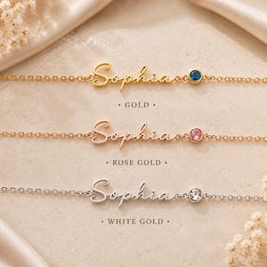 May include: Three delicate chain bracelets featuring the name Sophia in cursive script. The top bracelet is gold with a blue stone, the middle is rose gold with a pink stone, and the bottom is white gold with a clear stone. Text labels read Gold, Rose Gold, and White Gold.