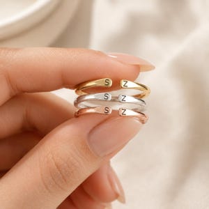 Puede incluir: Tres anillos abiertos apilados verticalmente, con un acabado en tono dorado, plateado y oro rosa. Cada anillo está grabado con las letras S y Z en los extremos de la banda, creando un aspecto personalizado para estos accesorios de metal.
