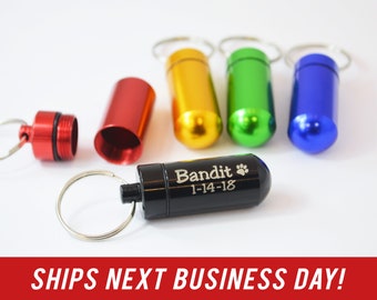 May include: Five small metal pill containers with key rings. The containers are red, yellow, green, blue, and black. The black container has the text "Bandit 1-14-18" engraved on it.