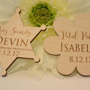 May include: Two wooden signs, one shaped like a star and the other like a flower. The star sign says "Ring Security Devin 8.12.17" and the flower sign says "Petal Patrol Isabella 8.12.17".