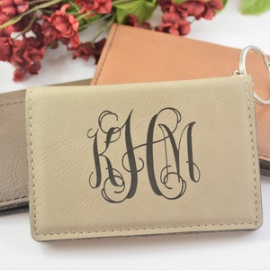 May include: Three leather keychains with a metal ring. The keychain in the center is beige and has the monogram "KHM" in a script font. The keychain on the left is brown and the keychain on the right is orange.