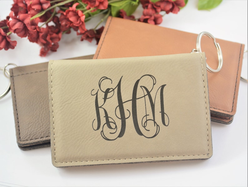 May include: Three leather keychains with a metal ring. The keychain in the center is beige and has the monogram "KHM" in a script font. The keychain on the left is brown and the keychain on the right is orange.