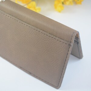 May include: A brown leather wallet with a key ring attached. The wallet has a fold-over design and a stitched seam.