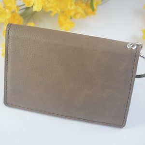 May include: A brown leather wallet with a silver key ring attached. The wallet has a stitched edge and a smooth, textured surface.