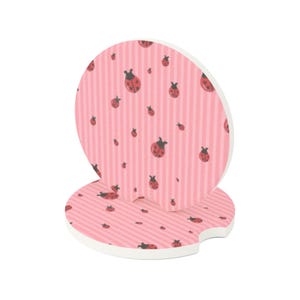 May include: Two circular car cup holder coasters featuring a light pink background with vertical stripes and a repeating pattern of small red and black ladybugs. Each coaster has a small semi-circular notch cut out from the edge of the disc.
