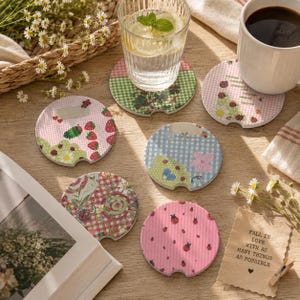 May include: A set of six round ceramic car coasters featuring various patterns including pink and blue gingham, strawberries, ladybugs, and flowers. One coaster has a cutout notch. A small paper note reads: FALL IN LOVE WITH AS MANY THINGS AS POSSIBLE.