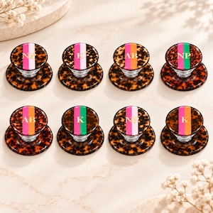 May include: Eight circular phone grips with a brown tortoiseshell pattern. Each grip features a vertical stripe in pink, orange, or green, and gold-colored monogram letters including NP, K, or AB printed in the center of the stripe.