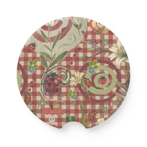 May include: A circular car coaster featuring a red and white gingham check pattern decorated with illustrations of ladybugs, white lily flowers, green leaves, small blue and green flowers, concentric circles, and a small apple core graphic.