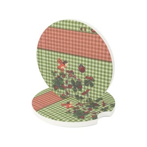 May include: Two round car coasters featuring a green and white gingham pattern with a horizontal coral stripe. The design includes illustrations of small red ladybugs, green clover leaves, and tiny red berries scattered across the surface.
