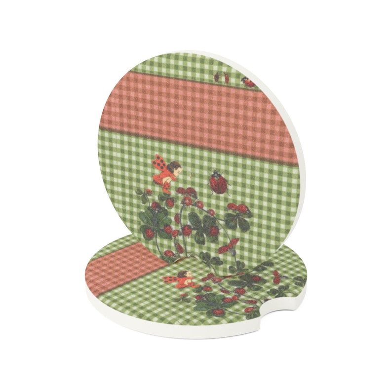 May include: Two round car coasters featuring a green and white gingham pattern with a horizontal coral stripe. The design includes illustrations of small red ladybugs, green clover leaves, and tiny red berries scattered across the surface.