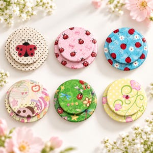 May include: Six circular decorative buttons featuring ladybug motifs. The designs include polka dots, pink with bows, blue with flowers, abstract patterns, green with dragonflies, and yellow with swirls. Each button has a smaller circular center.
