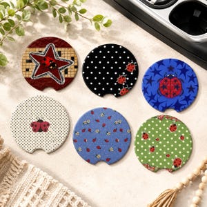 May include: Six circular car cup holder coasters featuring various designs: a red star on a grid, black with white polka dots and ladybugs, blue with stars and a ladybug, white with black dots and a ladybug, blue with flowers and ladybugs, and green with white dots and ladybugs.