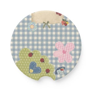 May include: A circular car coaster featuring a light blue and white gingham pattern. The design includes a beige rectangular label, a green scalloped shape with red ladybugs and a blue heart, a pink checkered flower, and small fruit motifs.