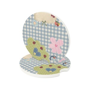 May include: Two round ceramic car coasters featuring a light blue and white gingham pattern. The design includes green cloud-shaped motifs with red ladybugs, blue hearts, pink checkered flowers, and small strawberry illustrations on a white base.