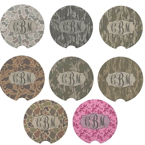 May include: A collection of seven car coasters with various camouflage patterns, including shades of green, brown, and pink. Each coaster features a monogram with the letters "CBM" in a decorative font.