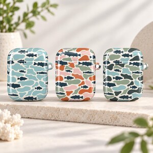 May include: Three protective cases for wireless earbuds, each featuring a repeating pattern of dark blue fish silhouettes layered over irregular, multi-colored organic shapes in shades of light blue, orange, pink, green, and dark teal.