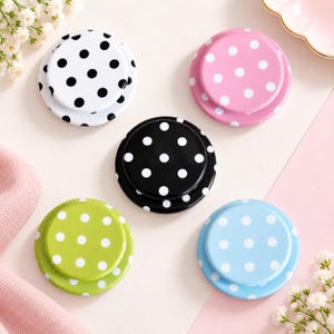 May include: Five circular phone grips arranged in a cluster. The top left grip is white with black polka dots. The top right is pink with white dots. The center grip is black with white dots. The bottom left is lime green with white dots, and the bottom right is light blue with white dots.