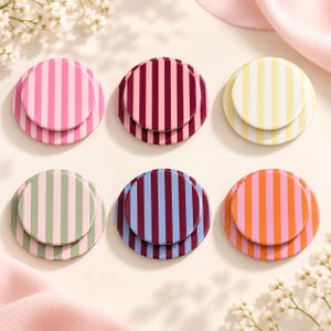 May include: Six circular phone grips arranged in two rows, each featuring a distinct vertical striped pattern. The colors include pink and light pink, dark red and maroon, yellow and white, sage green and light pink, blue and maroon, and orange and pink.