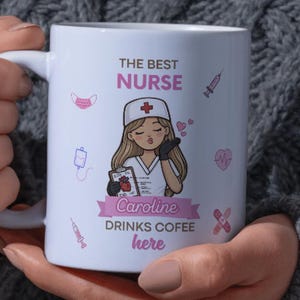 May include: White ceramic mug featuring a cartoon nurse illustration with the text "THE BEST NURSE" and "Caroline DRINKS COFEE here". The design includes medical symbols and a pink heart.