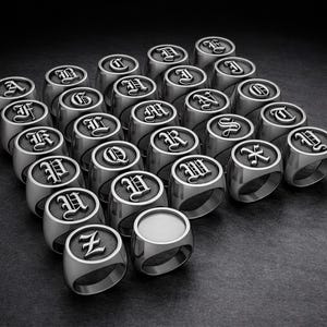 May include: A collection of silver-colored signet rings, each engraved with a different letter of the alphabet in a gothic font. The rings are arranged on a dark surface, creating a striking display of personalized jewelry.