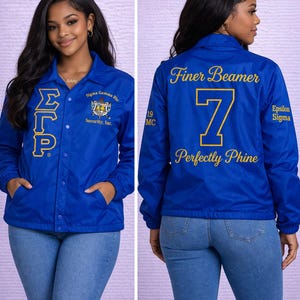 May include: A royal blue snap-front coach jacket featuring gold embroidery. The front displays the Greek letters ΣΓΡ and the Sigma Gamma Rho Sorority, Inc. crest. The back features the text Finer Beamer, the number 7, and Perfectly Phine.