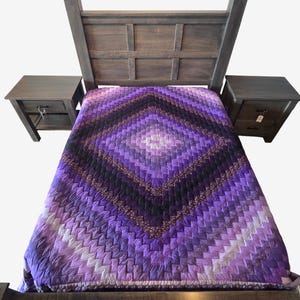 May include: A bed with a wooden frame and two matching nightstands. The bed is covered with a purple, black, and white patterned quilt. The quilt has a diamond design. The nightstands have drawers and are made of wood.