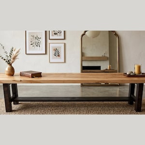 Peut inclure: Une grande table à manger rectangulaire en bois clair avec des pieds foncés. Elle est posée sur un tapis tissé. Des éléments décoratifs, comme un vase, un livre et un plateau avec une bougie, sont disposés sur la table. La pièce est de couleur neutre.
