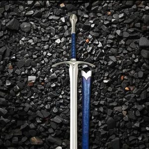 Könnte beinhalten: Ein silbernes Schwert mit blauem Griff und passender Scheide. Das Schwert hat eine lange, zweischneidige Klinge und einen Parier. Der Griff ist mit blauem Material umwickelt. Die Scheide ist blau mit einem weißen Design.
