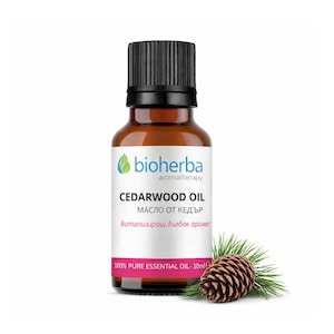 Op de afbeelding: Een bruine glazen flesje Cederhoutolie met een zwarte dop, een wit etiket en een dennenappel. Het etiket leest "bioherba aromatherapy CEDARWOOD OIL" en "100% PURE ESSENTIAL OIL - 10ml".
