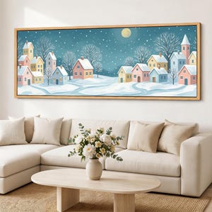 May include: A panoramic wall art print featuring a winter village scene with pastel-colored houses, snow-covered roofs, and bare trees under a dark teal night sky with a pale yellow moon and falling snow, all enclosed in a light wood frame.
