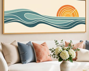 Op de afbeelding: Een ingelijste canvas print met een minimalistisch ontwerp van oceaangolven in blauwtinten en een oranje ondergaande zon. Het kunstwerk wordt weergegeven boven een witte bank met decoratieve kussens.