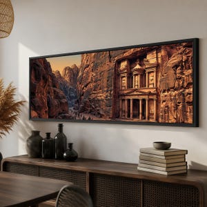 May include: A panoramic wall art print featuring the Treasury at Petra carved into orange sandstone cliffs. The scene depicts the ancient architectural facade with columns and intricate details set within a narrow canyon under a warm golden sky.