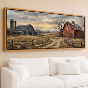 May include: A framed landscape painting depicts a rural scene with a red barn, gray barn, and silo under a cloudy sky. A dirt road leads through a field with a wooden fence. The artwork is displayed above a white sofa.