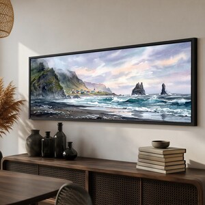 May include: A panoramic landscape painting in a black frame depicting a coastal scene with dark rocky cliffs, a small village with colorful houses, crashing ocean waves, and two prominent sea stacks under a soft, cloudy, pastel-toned sky.